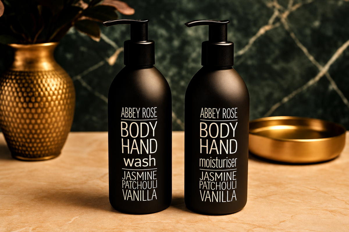 Two black bottles of Abbey Rose Body Hand wash and moisturiser on a wooden surface with decorative items in the background.